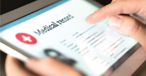 A doctor’s hands holding a tablet device while reviewing patient data.