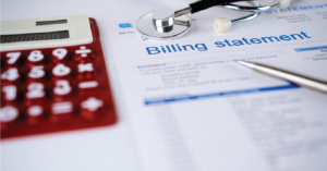 Medical patient statements on a table with a doctor’s stethoscope, a pen, and a calculator.