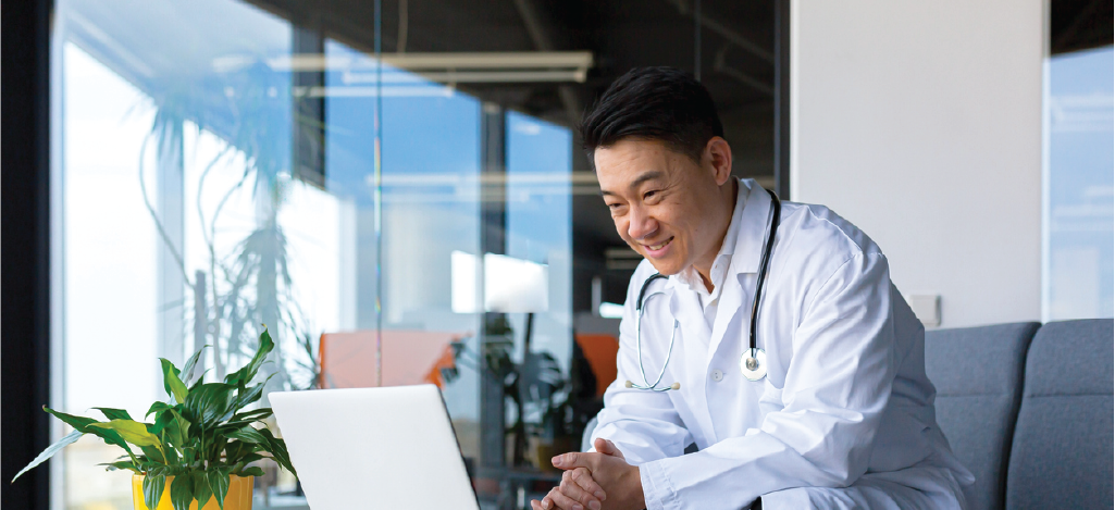 Male doctor using a laptop while speaking with his patient online.
