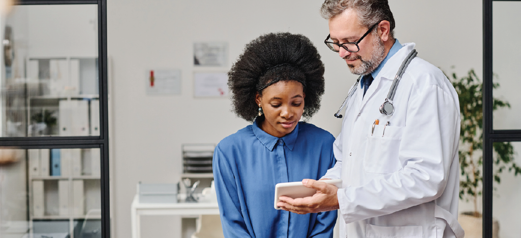 Male doctor showing medical records to a female patient using a tablet device.