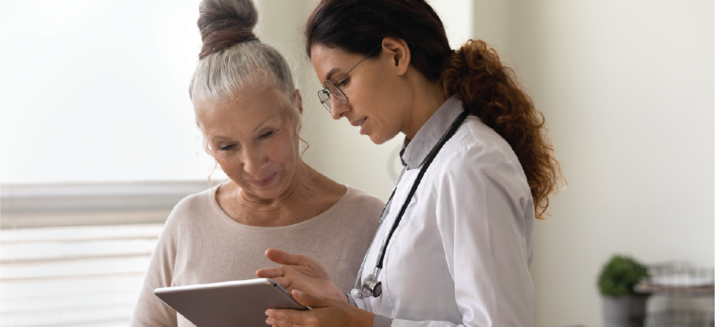 Female doctor using a tablet device to explain a senior woman’s medical bill.