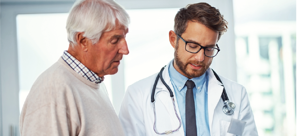 Using Electronic Remittance Advice - Male doctor holding a tablet device while assessing a senior patient’s insurance claim.