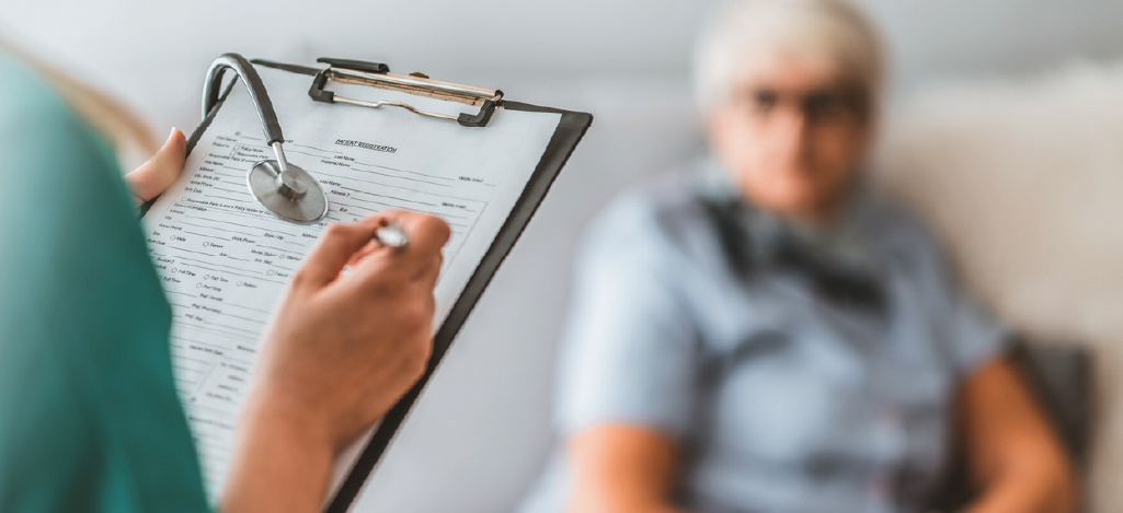 Doctor filling out a patient information form in front of a senior woman.
