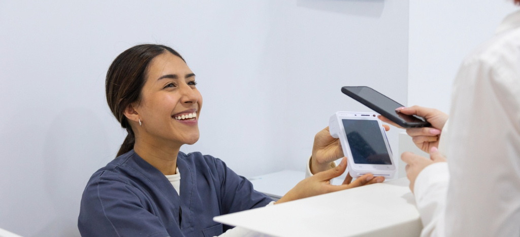 A female hospital staff member assisting a patient who is using her smartphone to pay for her medical bill.