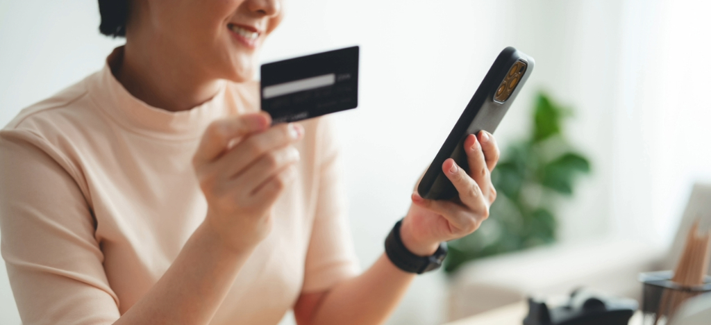 Billing experience strategies - A woman at home paying her medical bills using her smartphone and credit card.