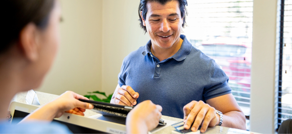 A female medical professional assisting a male patient in paying for his medical bill.