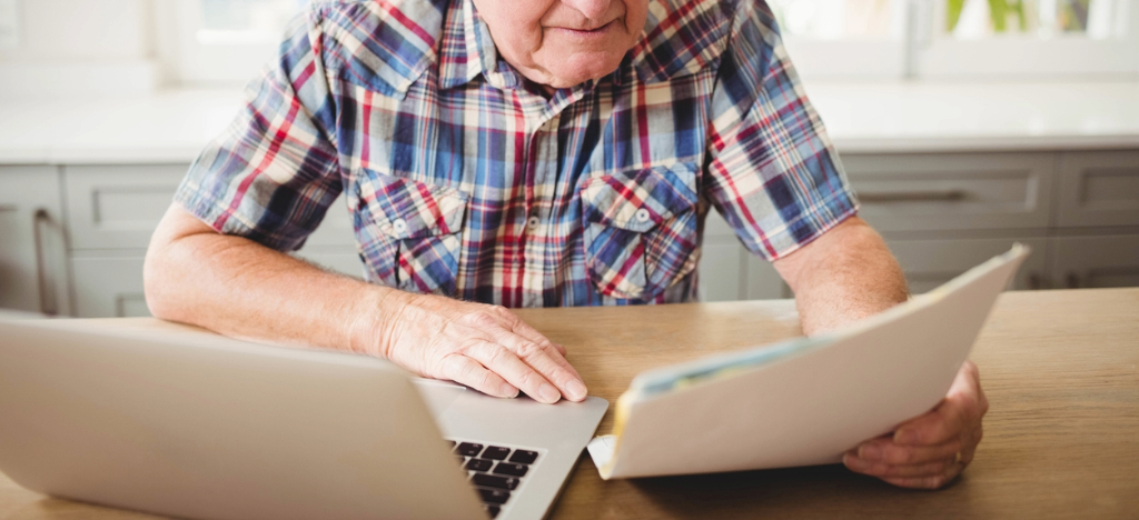 Using paper and electronic billing - A senior man at home looking at his printed hospital bill.