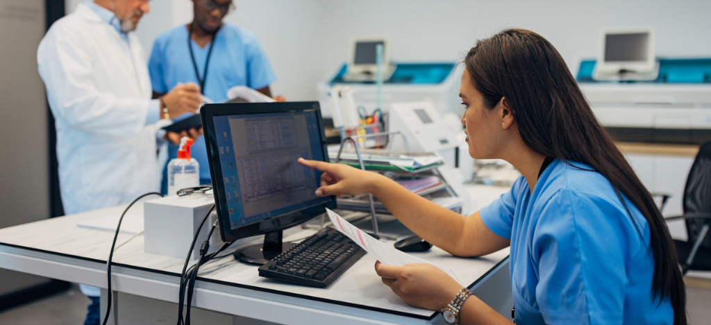 Medical billing software systems - A female medical staff member checking a printed medical bill and a digital copy shown on a computer.