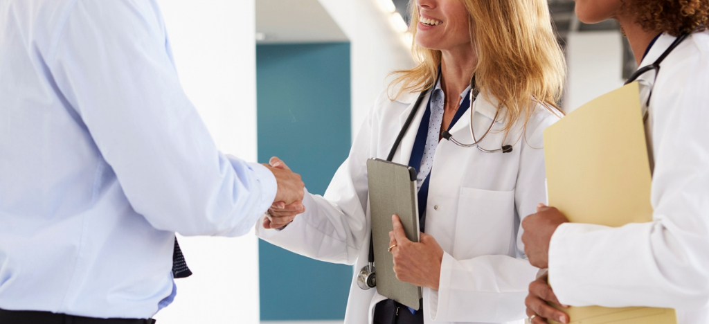 Outsourcing revenue cycle management - A female doctor shaking hands with a business partner.