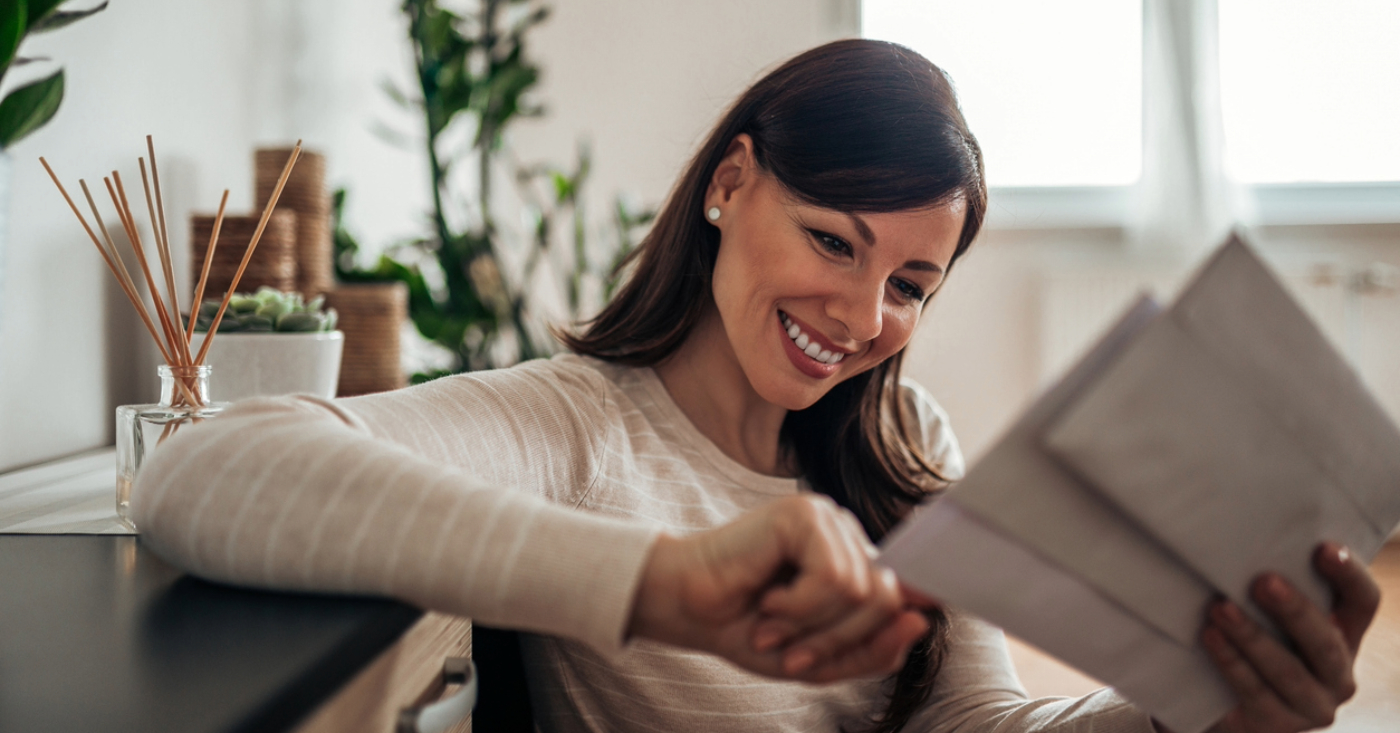 Creating direct mail inserts - A woman at home smiling as she checks inserts mailed by her medical provider.