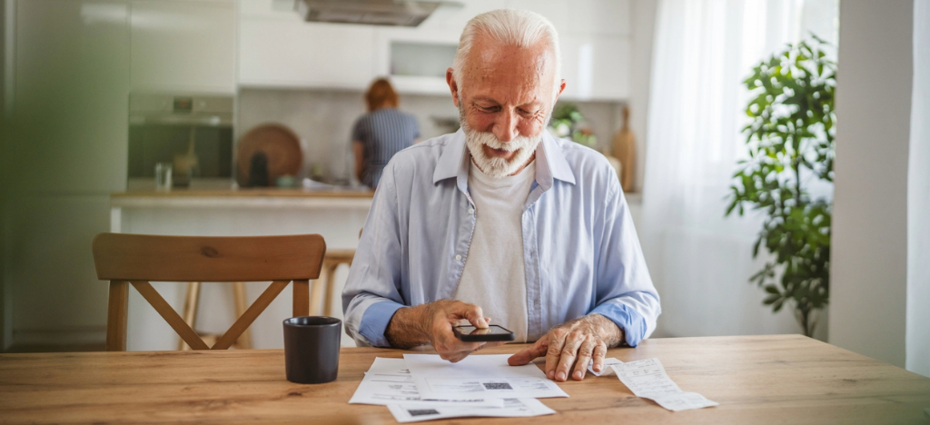 Direct mail inserts - A senior man at home using his smartphone to scan a QR code printed on his medical bill.