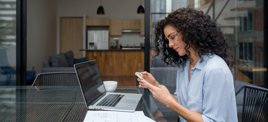 Medical billing software systems - A woman at home checking her medical bill using a smartphone and a laptop.
