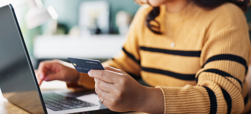 Payments for infusion centers - A woman at home holding a credit card and using a laptop to pay for her healthcare bills.