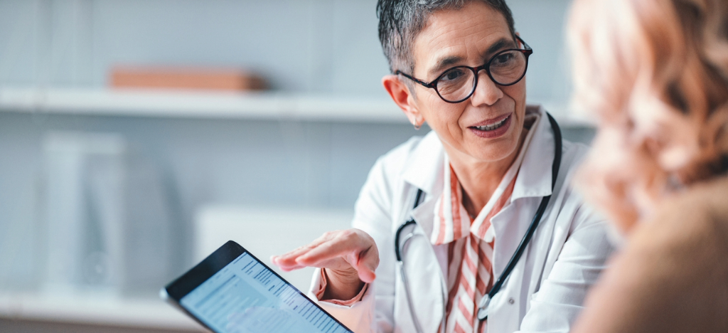 Medical debt collection - A female doctor holding a tablet device while explaining financing options to her patient.
