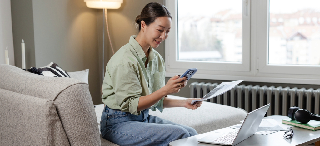 A woman at home paying her medical bills using her smartphone and laptop.