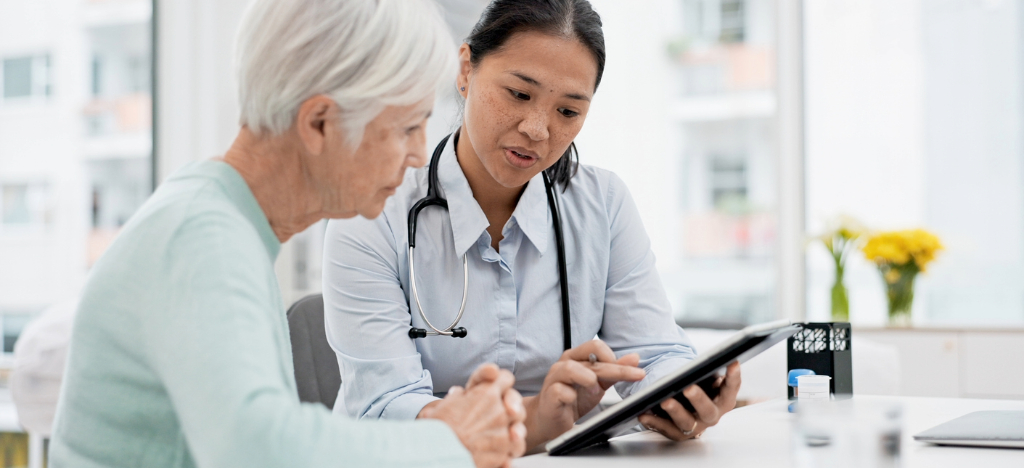 Patient communication platforms - A female doctor using a tablet device to explain payment options to her female senior patient.