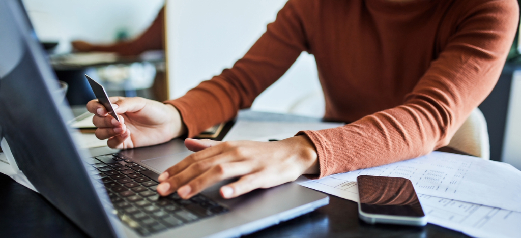 A woman at home using a laptop and a credit card to pay for her medical bills.