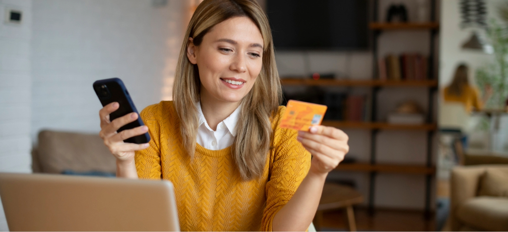 A woman at home using her credit card, smartphone, and laptop to pay for her medical bills.