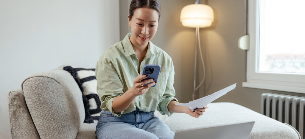 Medical billing best practices - A woman at home paying her medical bills using a smartphone and laptop.