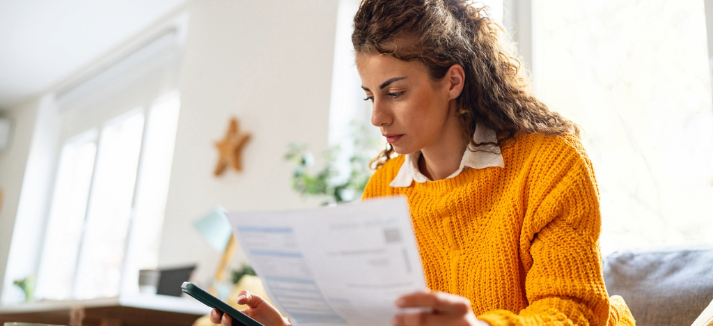 Pairing a paper statement with digital solutions - A woman at home holding a mailed medical bill while paying charges using her smartphone.