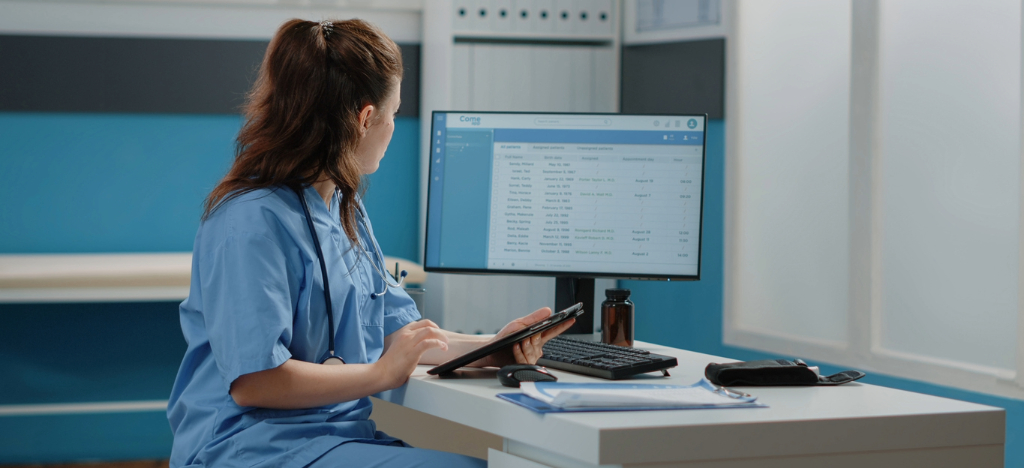 A female medical office staff member using a tablet device and a computer to manage patients’ medical bills.