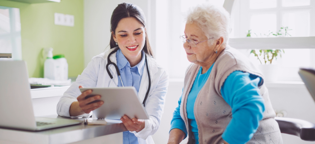 Managing patient surge - A female doctor using a tablet device while reviewing payment options with her senior patient.
