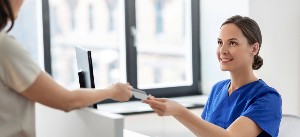 Improving medical debt collection - A female medical staff member assisting a woman in paying her medical bill.