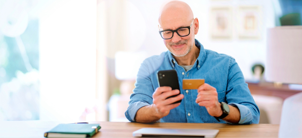 A man at home using his smartphone and credit card to pay for his medical bill.
