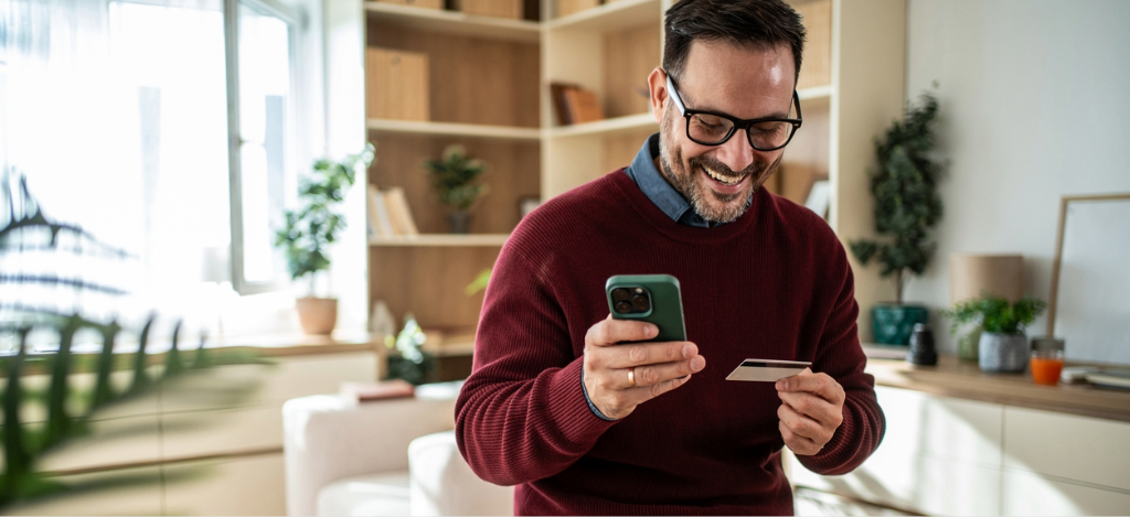 Patient payment plan - A man at home using his smartphone and credit card to pay for his hospital bills.