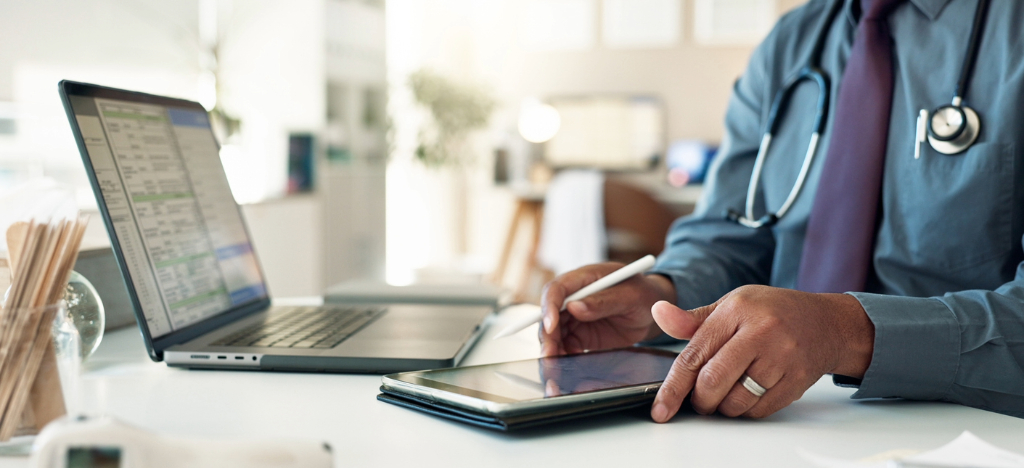 Merchant accounts processing - A male doctor accessing medical billing software on a tablet device and a laptop.