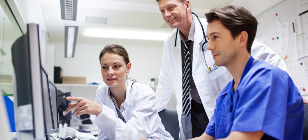 Billing strategy - A group of doctors looking at computers while discussing hospital billing operations.