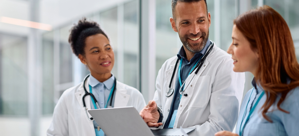 Tracking in-office payment processes - A male doctor holding a laptop while discussing hospital revenue with his colleagues.