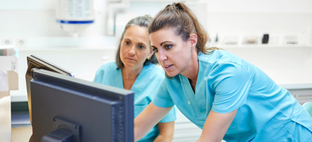 Using smarter medical billing systems - Two female hospital staff members using a computer to check patients’ medical bills.