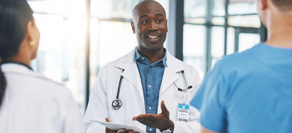 Managing patient surge - A male doctor holding a tablet device while explaining year-end operations to his colleagues.